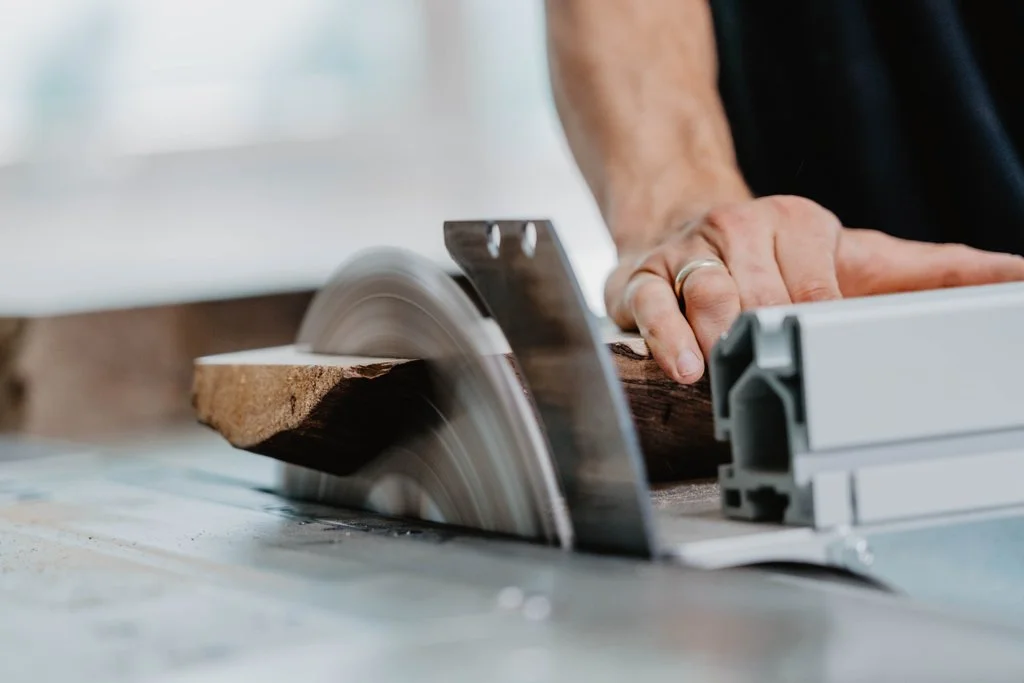 Hände führen Holz durch die Tischkreissäge in der Werkstatt
